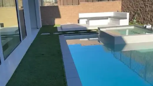 A clean, turquoise-blue pool sits next to a verdant patch of grass.